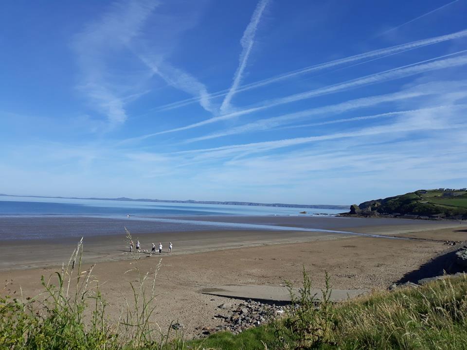 Looking north across Broad Haven beach with lots of vapour trails criss-crossing the blue sky