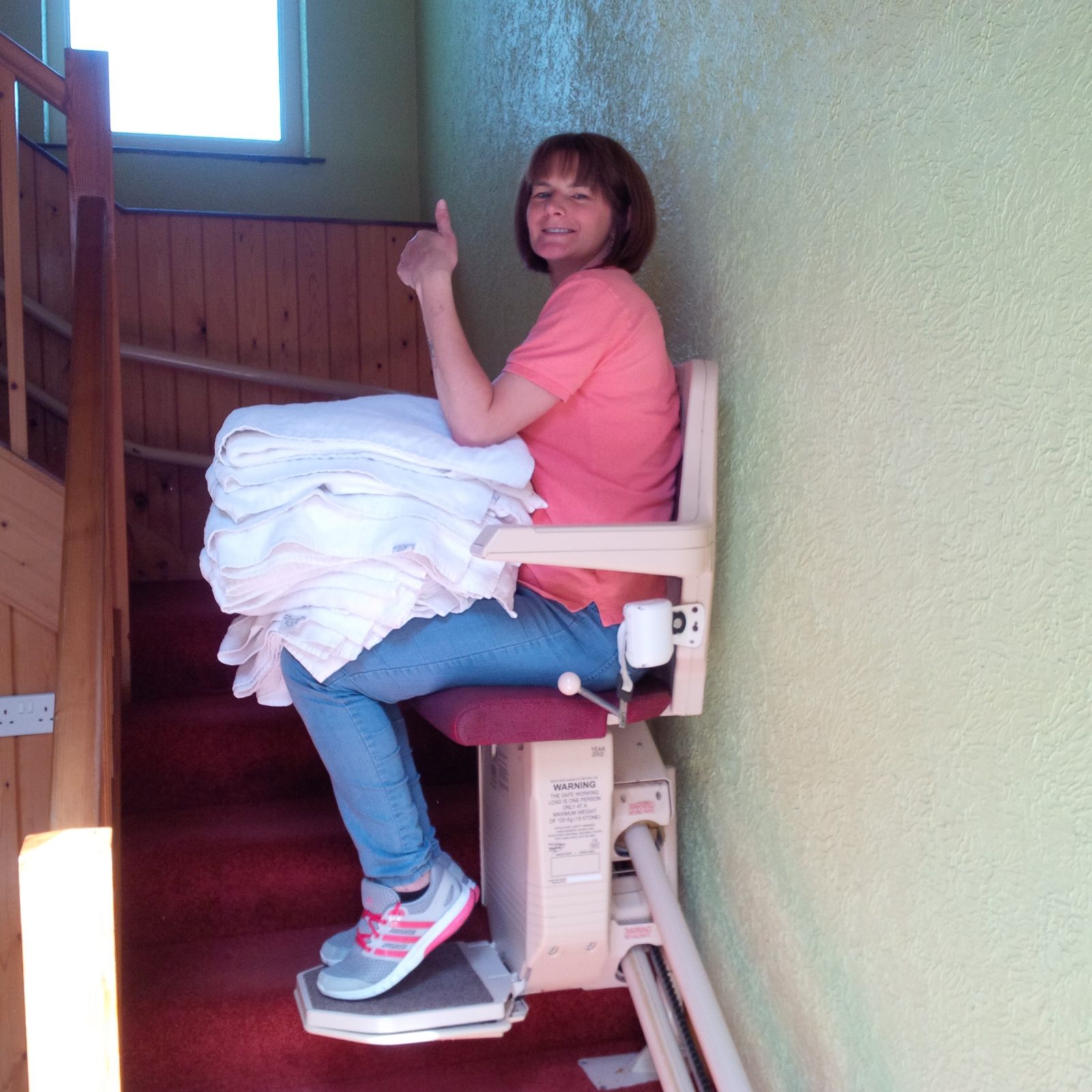 A cleaner carries bedding and towels on the stairlift in apartment 2