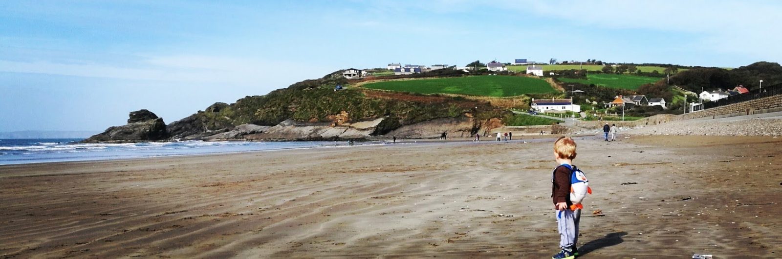 A panoramic view of Broad Haven beach showing a two year old gazing at all the space.